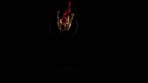 Девушка выполняет акробатические элементы в воздушном кольце. Чёрный фон — стоковое видео