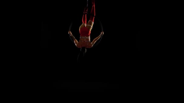 Гимнаст висит вверх ногами на воздушном обруче. Чёрный фон — стоковое видео