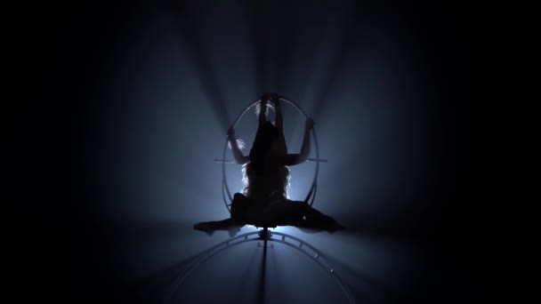 女の子の空気のアクロバットは、フープの上に座っている間、空気中で回転します。黒の煙の背景。シルエット — ストック動画