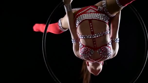 Девушка-спортсмен в красном костюме выполняет акробатические трюки на воздушном обруче. Чёрный фон. Медленное движение. Закрыть — стоковое видео