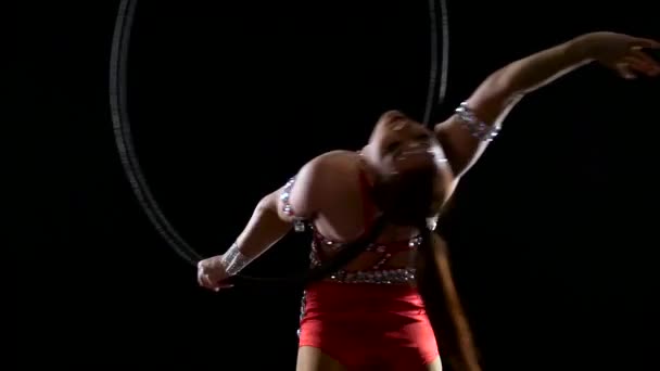 Девушка-спортсмен в красном костюме выполняет акробатические трюки на воздушном обруче. Чёрный фон. Медленное движение. Закрыть — стоковое видео