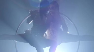 Hava akrobatlar kızlar metal bir çember üzerinde havada döndürün. Siyah duman arka plan. Siluet. Yavaş hareket. Yakın çekim