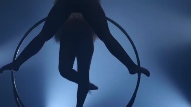 Hava akrobatlar kızlar metal bir çember üzerinde havada döndürün. Siyah duman arka plan. Siluet. Yavaş hareket. Yakın çekim