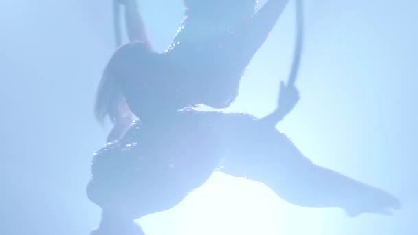 Girls rotate gracefully in the air while sitting on a metal hoop. Black smoke background. Silhouette. Slow motion. Close up — Stock Video