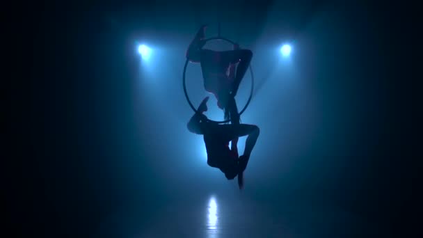 As meninas de acrobatas aéreas giram graciosamente no ar um aro metálico. Fundo de fumo preto. Silhueta. Movimento lento — Vídeo de Stock