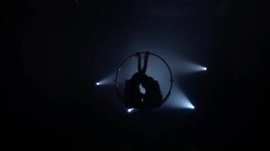 Bir çember üzerinde sallanan ve hava çember üzerinde jimnastik unsurları yapma. Siyah duman arka plan. Siluet. Yavaş hareket