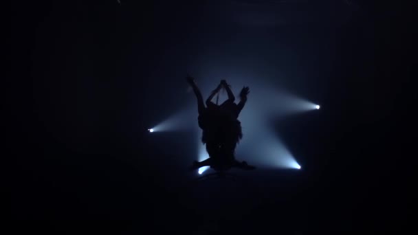 Two girls rotating on a metal hoop in dark room . Black smoke background. Silhouette. Slow motion — Stock Video