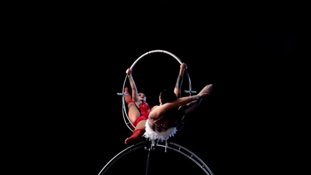 Two girls aerialists spinning on a hoop on stage. Black background. Slow motion — Stock Video