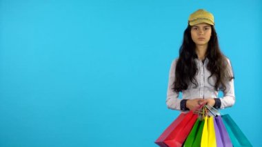 Elinde torbalar ile alışverişkolik kız ayakta ve gülümsüyor başlar. Mavi arka plan