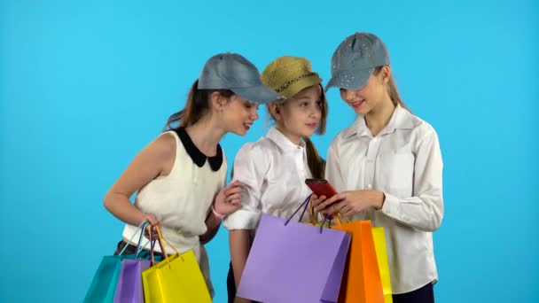 Three teenagers make selfies with colorful packages. Blue background — Stock Video