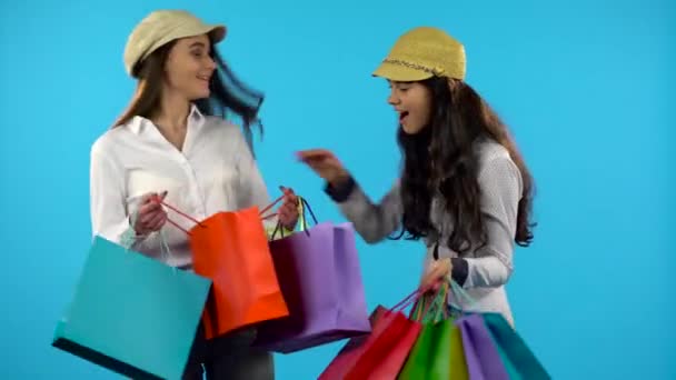 Dos niñas sonrientes felices sostienen bolsa de compras. Fondo azul — Vídeo de stock