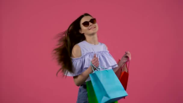 Chica en gafas de sol bailando con paquetes en sus manos. Fondo rosa — Vídeos de Stock