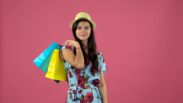 Shopaholic dívka s taškami v ruce stojí a začíná s úsměvem. Růžový pozadí. Zpomalený pohyb — Stock video