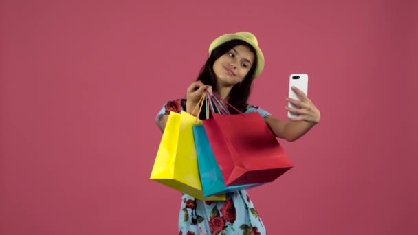 Adolescente hacer selfies con paquetes de colores. Fondo rosa. Movimiento lento — Vídeo de stock
