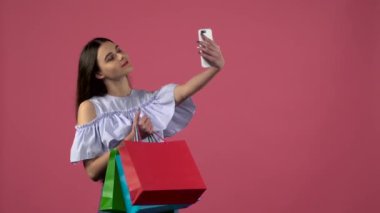 Kız selfies renkli paketleri ile olun. Pembe bir arka plan. Ağır çekim
