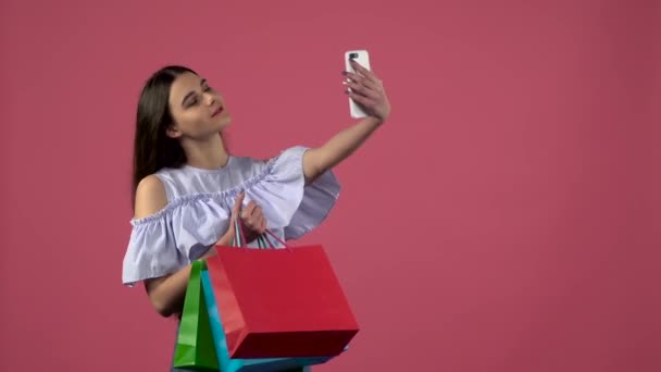 Flicka gör selfies med färgglada paket. Rosa bakgrund. Slow motion — Stockvideo