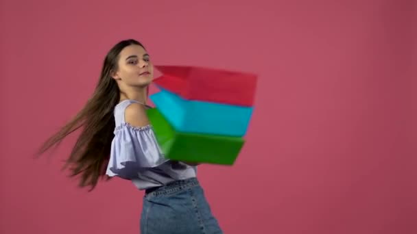Mädchen mit Einkaufstüten, den Kopf verdreht und zwinkernd. rosa Hintergrund. Zeitlupe — Stockvideo