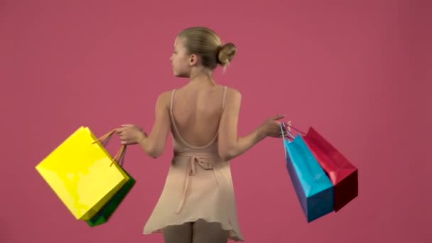 Dançarina infantil girar com sacos de compras em suas mãos. Fundo rosa. Movimento lento — Vídeo de Stock