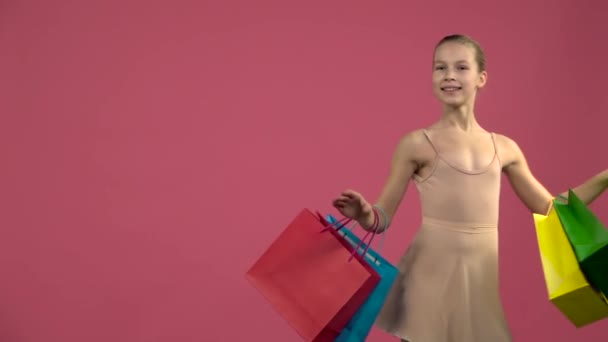 Dançarino em traje girando ao redor com sacos de compras multicoloridos. Fundo rosa. Movimento lento — Vídeo de Stock