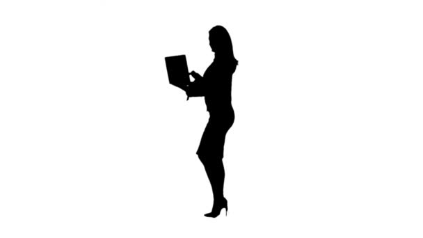 La mujer de negocios camina con un portátil en la mano e imprime un mensaje. Vista lateral. Fondo blanco. Silueta. Movimiento lento — Vídeos de Stock