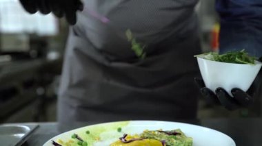 Siyah eldivenli şef, maşalı kreplere yeşillik koyar.