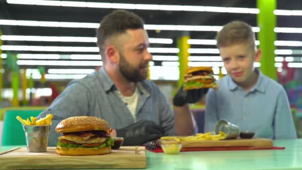 Restoranda hamburger yiyen baba ve oğulun yavaş hareketi. — Stok video