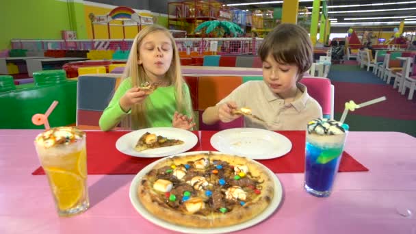 Vrolijke kinderen genieten van chocolade pizza tijdens het diner op entertainment Park. — Stockvideo