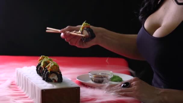 Fille appréciant des sushis servis dans la fumée par des baguettes sur le fond noir. — Video