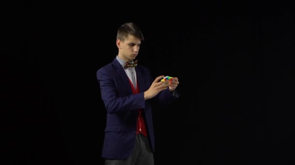 Unsmile homem de terno está resolvendo Rubiks Cubo no escuro . — Vídeo de Stock