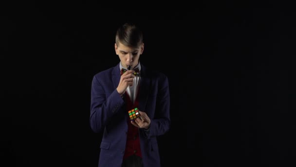 Chico serio en traje está resolviendo Rubiks Cube en la oscuridad . — Vídeos de Stock