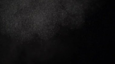 Yüzen minyatür toz parçacıkları siyah bir arka plan üzerinde süzülür.