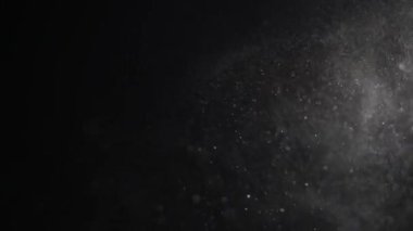 Yükselen küçük toz parçaları siyah arka plan üzerinde pırıl pırıl.