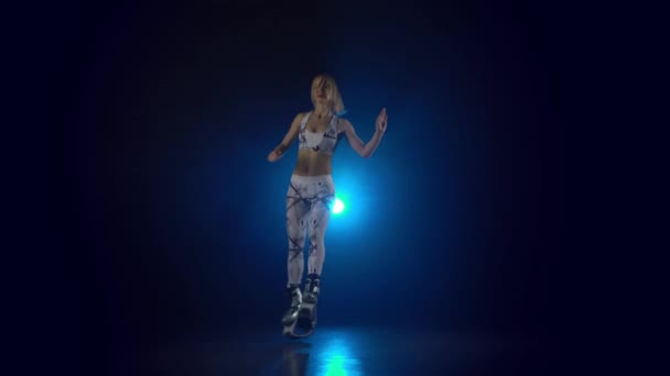 Kobieta tańczy w Kangoo skacze buty przed niebieskim reflektorem — Wideo stockowe