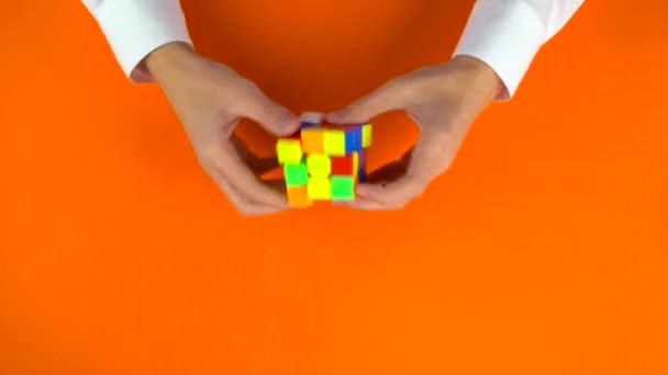 Ukraine, dnipro 20. Feb 2019: Jungs Arme lösen den Rubiks-Würfel schnell auf orangefarbenem Hintergrund. — Stockvideo