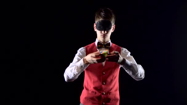 Ukrajina, Dnipro 20 únor 2019: muž s zavázanými oči v červené vestě řeší kostku Rubiks. — Stock video