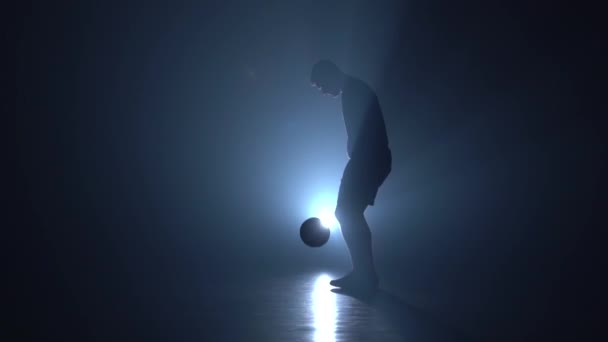 Силует футбольного фрілансера, що фарбує м'яч проти синього точкового світла. Повільний рух — стокове відео