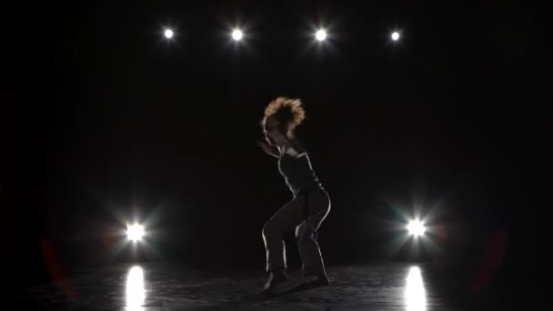 Morena mujer practicando capoeira en la oscuridad contra proyector en estudio . — Vídeo de stock