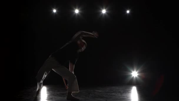 스튜디오에서 스포트라이트에 대한 어둠 속에서 카포에이라를 연습하는 남자. — 비디오