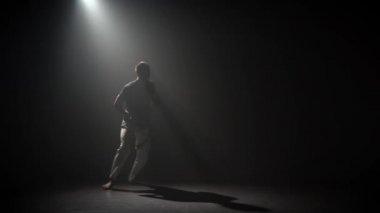 Adam stüdyoda spot altında karanlıkta capoeira pratik.