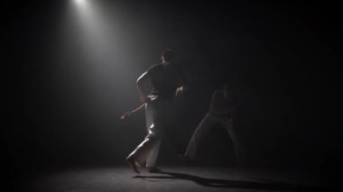 Yakışıklı erkekler stüdyoda spot karşı karanlıkta capoeira pratik.
