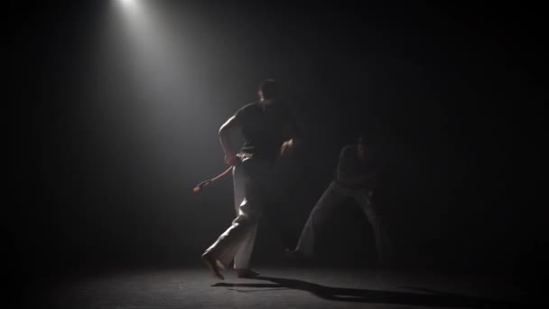 Beaux mâles pratiquant la capoeira dans l'obscurité contre les projecteurs en studio . — Video