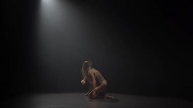 Spot ışığı altında karanlık stüdyoda tefekksyon dans eden kadın