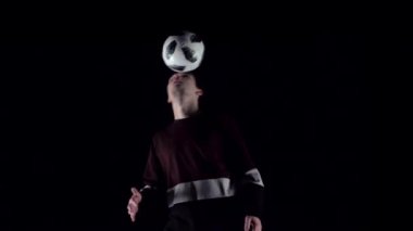 Futbol serbest stil. Karanlık stüdyoda topla numaralar yapan futbolcu. Yavaş çekim