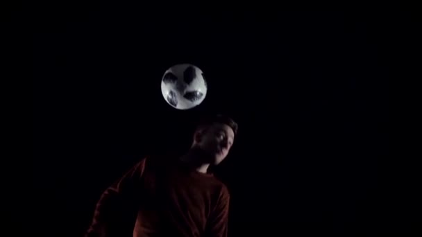 Estilo libre de fútbol. Primer plano jugador de fútbol haciendo trucos con la pelota en la cabeza en la oscuridad. Movimiento lento — Vídeo de stock