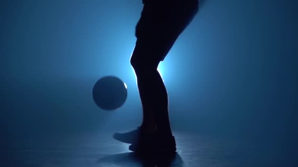 男性双腿的特写镜头将球塞在蓝色聚光灯下。慢动作 — 图库视频影像