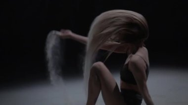 Karanlık stüdyoda toz parçacıkları atan kadın. Yavaş çekim