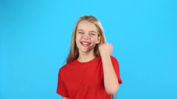 Petite blonde est heureuse de la victoire, elle danse avec bonheur sur fond bleu — Video