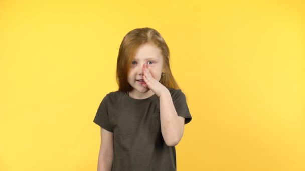 Рыжеволосый ребенок рассказывает секрет на желтом фоне — стоковое видео