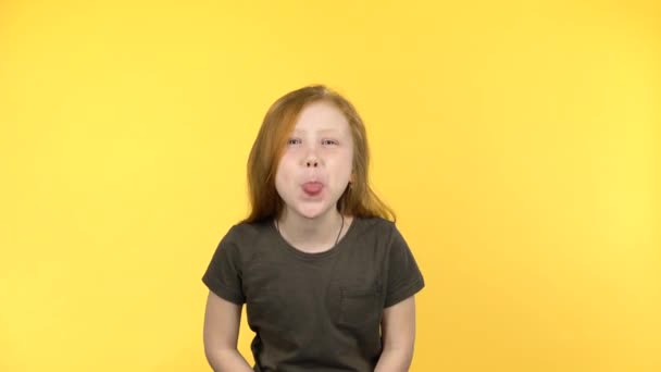 Funny red-haired girl smiles into the camera and shows tongue — Stock Video