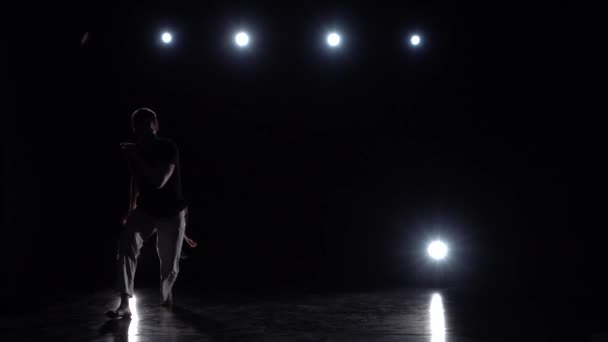 Homme sportif pratiquant la capoeira dans l'obscurité contre les projecteurs en studio . — Video